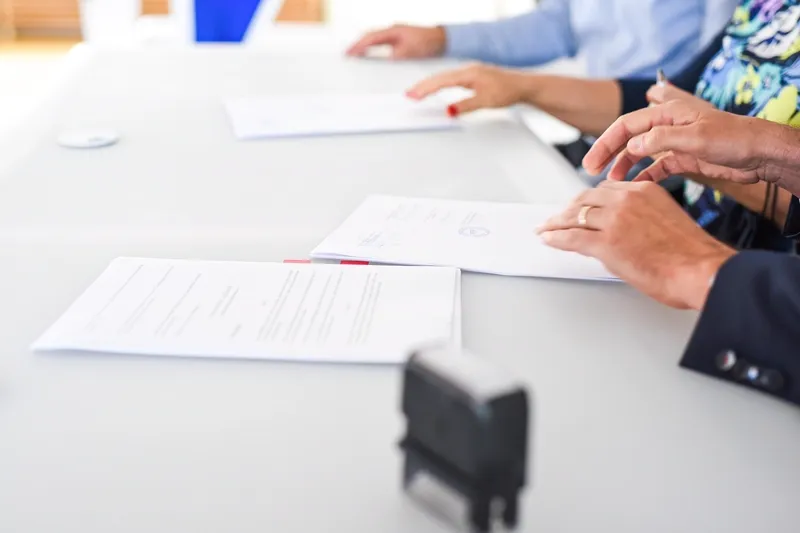 Mãos assinando contrato sobre uma mesa, representando a comparação entre financiar e dar o carro em garantia